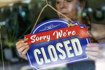 Sad Female Store Owner Turning Sign to Closed in Window