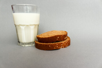  glass of milk with sliced dark ripe bread on grey background