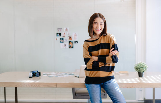 Smiling beautiful Asian woman photographer standing with arms crossed and looking away while work selecting best photos after process develop. Freelance Startup Small business owner,Online marketing.