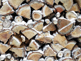 Stacked wood in the snow. Background of firewood with snow.