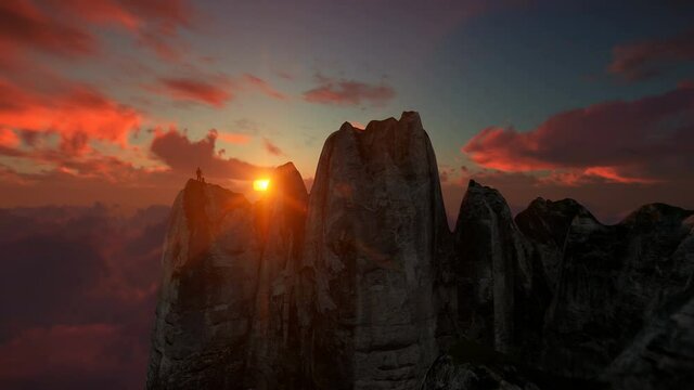 Hiker on top of a mountain above clouds against beautiful sunrise, drone view 4K