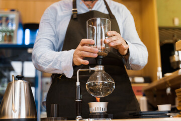 Barista holds Syphon device in hands before coffee brewing in cafe. Syphon alternative method of making coffee. Scandinavian method of coffee making.