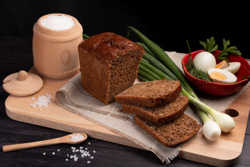 black bread on a linen napkin with green onions, eggs and salt in a wooden jar