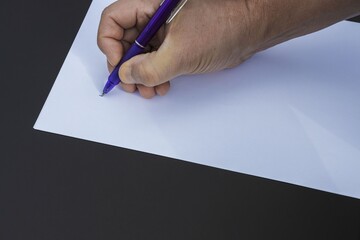 Close up view of male right hand writing on white peace of white paper.  