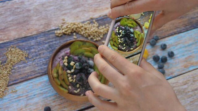 Female Foodie Hands Taking Photo Of Healthy Smoothie Bowl On Wooden Table Using Cellphone. 