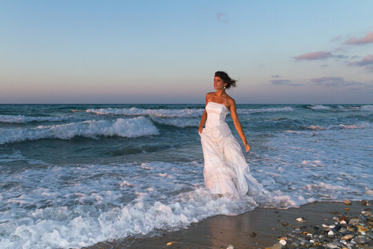 Young beutiful bride feeling free and happy, breathing clean fresh ocean air on a sandy beach in summer at dusk.