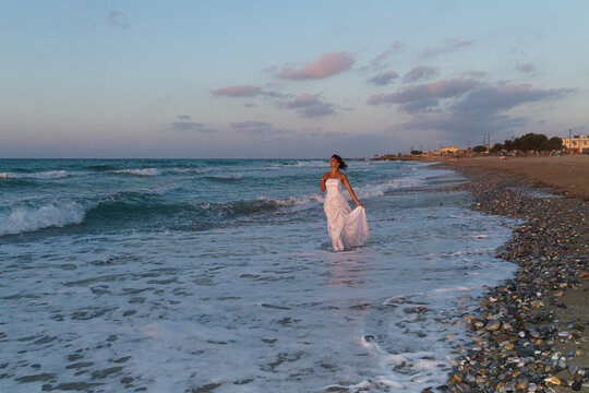 Young beutiful bride feeling free and happy, breathing clean fresh ocean air on a sandy beach in summer at dusk.