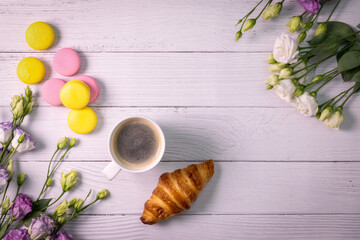 macarons and croissant with flowers and cup of coffee on white wooden background with copy space. top view