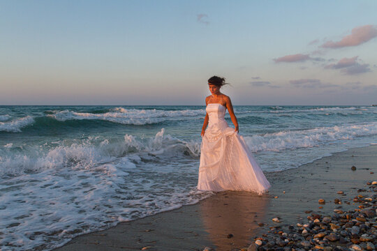 Young beutiful bride feeling free and happy, breathing clean fresh ocean air on a sandy beach in summer at dusk.