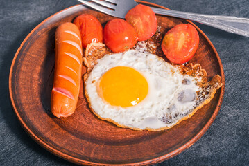 Easy quick breakfast - fried egg, tomatoes and sausage on a clay plate, top view, dark background