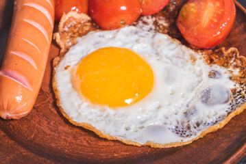Easy quick breakfast - fried egg, tomatoes and sausage on a clay plate, top view, close-up