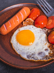 Easy quick breakfast - fried egg, tomatoes and sausage on a clay plate, top view, close-up