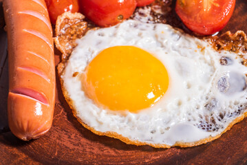 Easy quick breakfast - fried egg, tomatoes and sausage on a clay plate, top view, close-up
