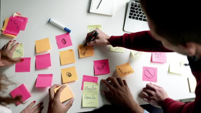 Creative business group brainstorming at workplace, writing and sticking notes on desk, planning and analyzing project. Top view, cropped shot. Teamwork and cooperation concept