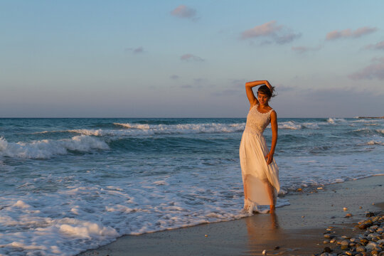 Backlit woman feeling free and happy, breathing clean fresh ocean air on a sandy beach in summer at dusk.