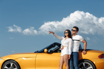 Positive young couple staying beside a yellow convertible car. Freedom, travel and love concept.