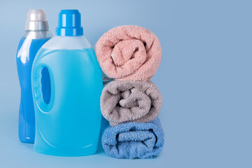 Obraz na płótnie Canvas Bottles of detergent and fabric softener with clean towels on blue background. Containers of cleaning products, household chemicals. Liquid detergent and conditioner. Laundry day, cleaning concept.