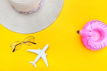 Summer beach composition. Minimal simple flat lay with plane sunglasses hat and Inflatable flamingo isolated on yellow background. Vacation travel adventure trip concept. Top view copy space.