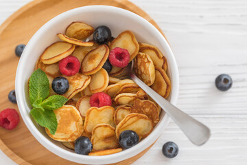 Bowl for breakfast with tiny pancake cereal with blueberries, raspberries, mint