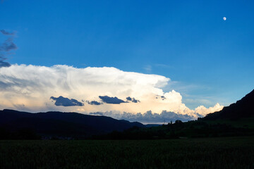 Huge white storm cloud moves over the Swabian alb. In the foreground the silhouette of trees and fields is visible, beautiful blue sky. Germany