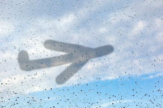 Picture of an airplane on misted glass. A window glass with raindrops against a sky. The concept of non-flying weather, flight delay.