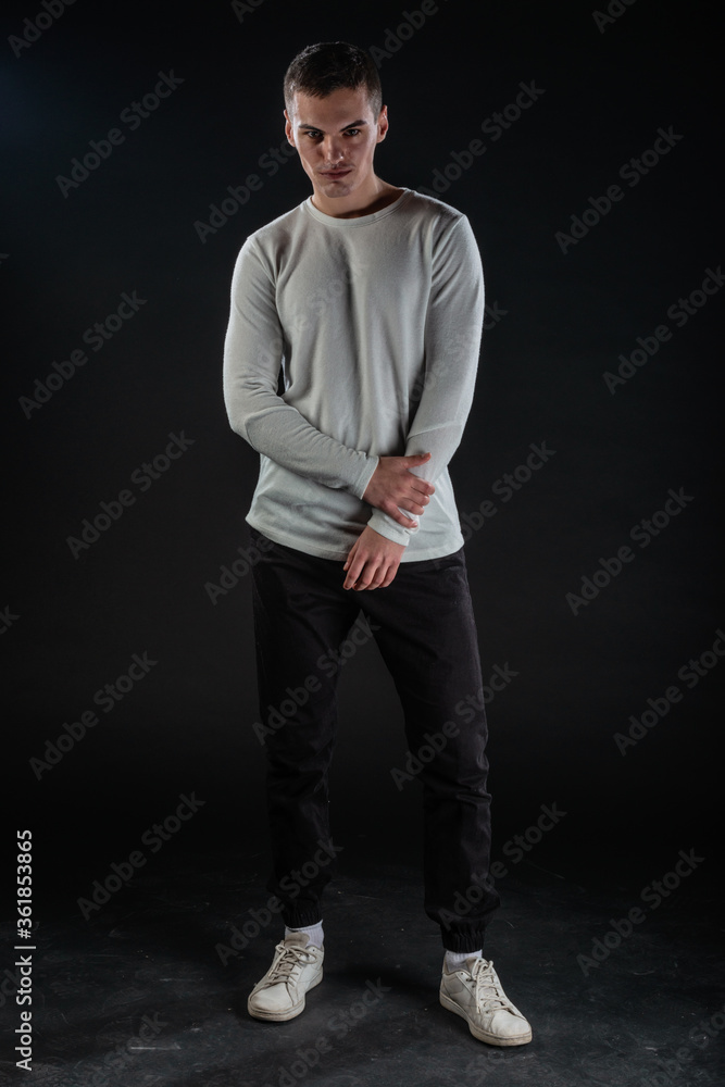 Poster Fashion portrait on a black background of a handsome male model in white blouse and black pants