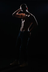 High contrast silhouette portrait of a sexy young male model shirtless posing on the side.
