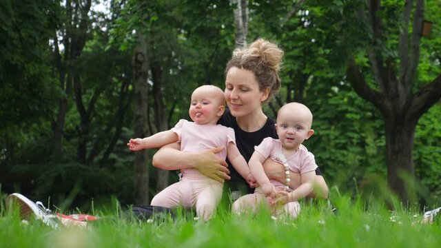 Mother Kissing Her Twin Babies Having Fun Outdoors In Park.
