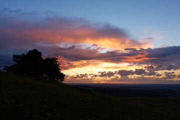 Sunset with blue sky and orange-gray clouds, the trees and meadow in the foreground are barely visible as a silhouette. Germany.