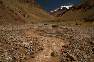 Seven summits. Rocky stream flowing downhill along the valley. Mountain Aconcagua, highest peak in America, in the background.