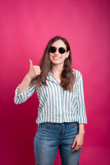 Cheerful young woman is showing like or thumb up gesture standing on the pink background