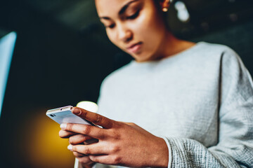 Pensive african american girl holding smartphone for chatting, selective focus on telephone in hand of young dark skinned  woman chatting social networks for chatting and sending messages online .