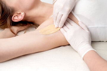Obraz na płótnie Canvas Hand of cosmetologist applying wax paste on armpit. Depilation or epilation female armpit with liquid sugar paste. Smooth underarm concept