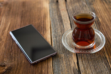 A glass of tea and mobile smart phone on the wooden background.