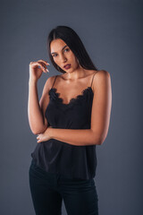 Fototapeta premium Sensual studio portrait of a sexy woman standing with one arm crossed on a gray background