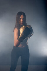 Fototapeta na wymiar Foggy image of a young and sexy female boxer punching direct hit with boxing gloves