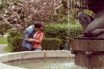 Young, happy, loving couple having date in the park near fountain. Relations, friendship and love.