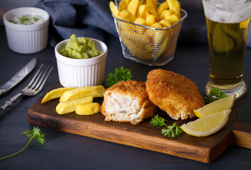 Battered fish with french fries, mushy peas and sauce. Fish and chips, glass of beer. Horizontal image