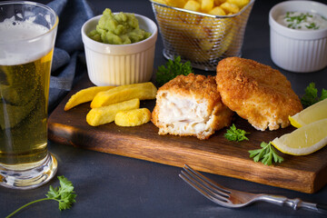 Battered fish with french fries, mushy peas and sauce. Fish and chips, glass of beer. Horizontal image