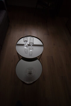 Two champane glasses in mirror coffe table in dark room with oak wood floor