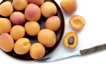 Ripe apricots in brown plate with knife on white background. Top view