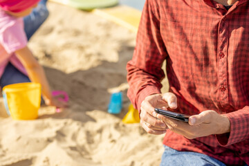 Dad looks at his phone and does not follow children in the playground