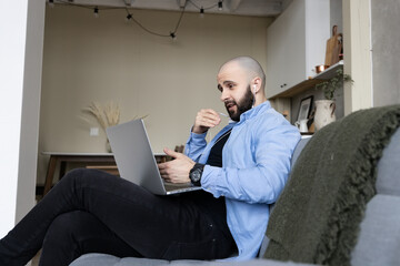 A brutal guy with a beard and a shirt participates in a video conference from home . Concept of work and study online