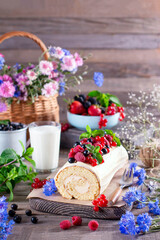 Biscuit roll with mascarpone cream and berries, mint leaves on wooden background.