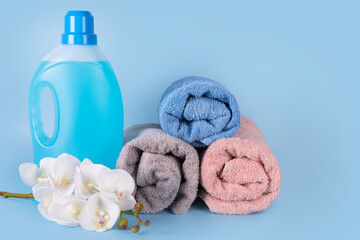 Obraz na płótnie Canvas Bottle of detergent with clean towels and flowers on blue background. Plastic container of cleaning product, household chemicals, liquid laundry detergent. Laundry day, cleaning concept. Copyspace