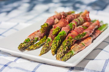 Green organic asparagus baked with bacon. Cooked Asparagus Officinalis on white plate on the table. Spring and summer vegetables for healthy snack. Recipe idea for branch.