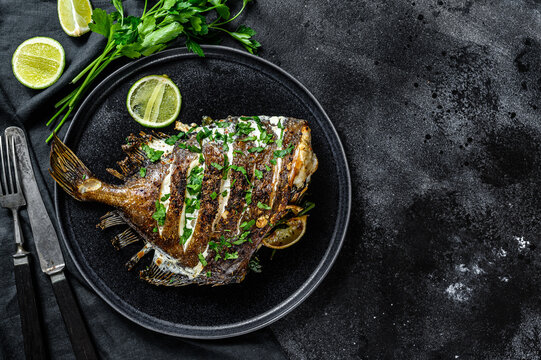 Grilled John Dory fish with lime and parsley in a pan. Black background. Top view. Copy space