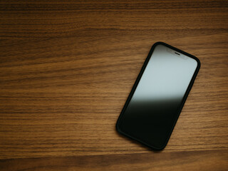 Top down view of iPhone sitting on a fine wood grain desk, either in the office or at home © Drew Woolery