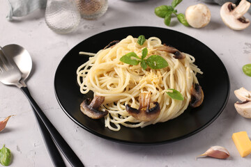 Spaghetti with mushrooms and basil on black plate on a gray background, Close-up, Horizontal format