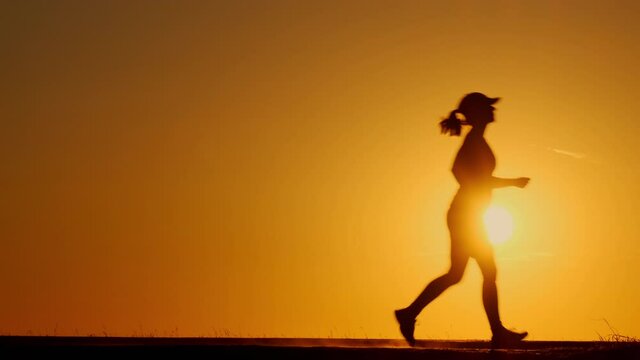 Silhouette of girl makes evening jog at sunset.